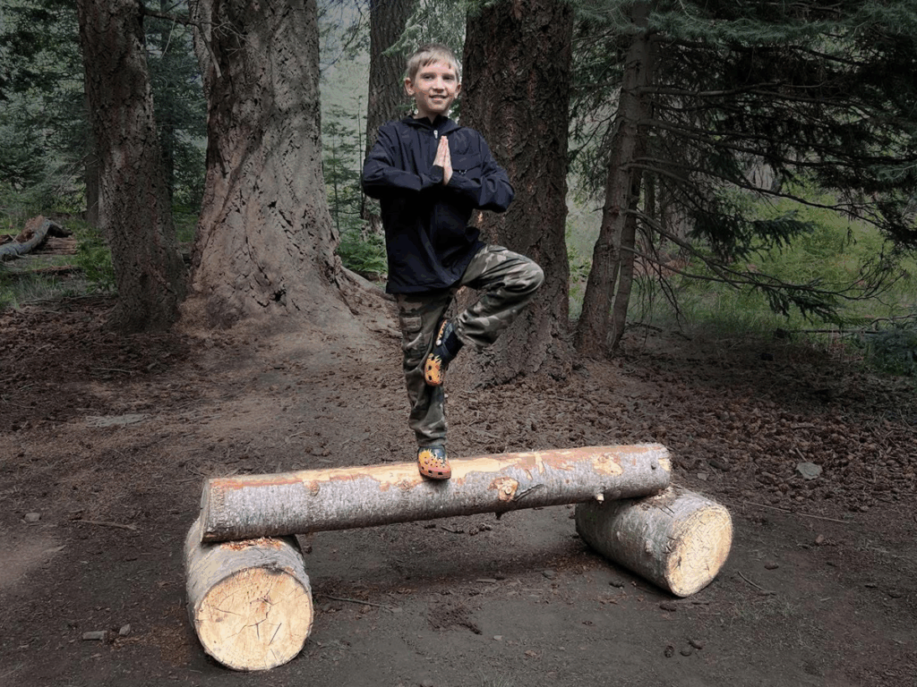 Child balancing on a log in the forest during a dojo camping trip, practicing focus and fun.